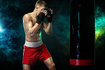 Sportsman, man boxer fighting in gloves with boxing punching bag. Isolated on black background with...
