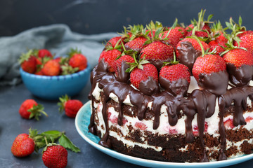 Chocolate cake with strawberries and cream located on a dark background