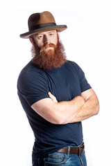 A young man with red hair and a full beard wearing a retro Homburg hat standing with arms crossed. Isolated on white.