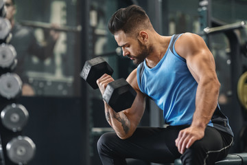 Fototapeta na wymiar Bodybuilder pumping his biceps with dumbbell in gym