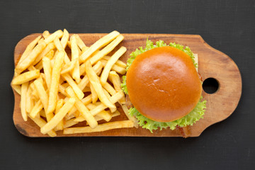 Hamburger and french fries on a rustic wooden board on a black background, overhead view. Flat lay, from above, top view. Close-up.