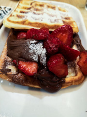 a waffle with strawberries, chocolate and sugar for the breakfast