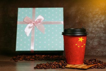 Paper cup for coffee with the image of the Chinese flag. Grains lie on a wooden surface.
