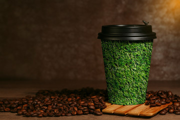 Eco friendly paper cup with takeaway coffee with picture of green grass placed on table with coffee beans in coffee shop