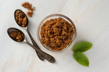 Brown sugar isolated in glass bowl, over styled marble background. Mint leaves. Top view, copy space.