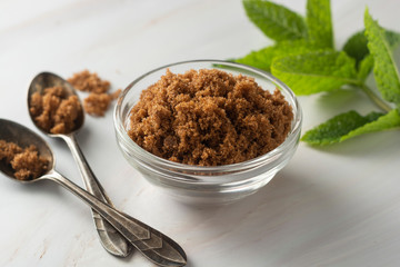 Brown sugar isolated in glass bowl, over styled marble background. Mint leaves. Top view, copy space.