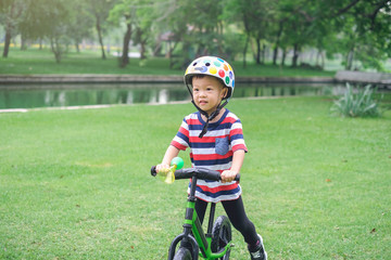 Cute little Asian toddler boy child wearing safety helmet learning to ride first balance bike in sunny summer day, kid playing & cycling at park