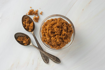 Brown sugar isolated in glass bowl, over styled marble background. Top view, copy space.