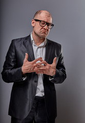 Unhappy doubt busuness man in black suit and glasses showing the palm refusing sign on grey...