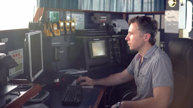 Marine navigational officer during navigational watch on Bridge . He works with paperjob on the computer. Modern work at sea