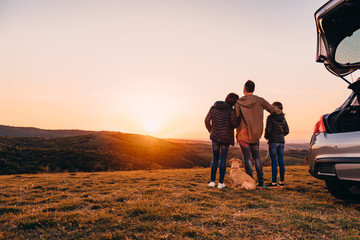 Family with dog embracing at hill and looking at sunset