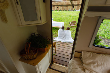 View from the door of the camper to a happy couple wrapped in a knitted blanket sitting next to the...
