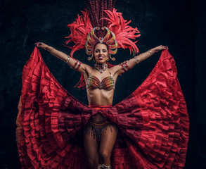 Talented joyful can can dancer in red feather costume is posing at small dark studio.