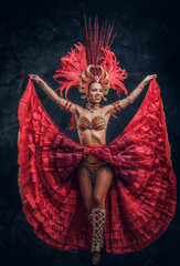 Talented joyful can can dancer in red feather costume is posing at small dark studio.