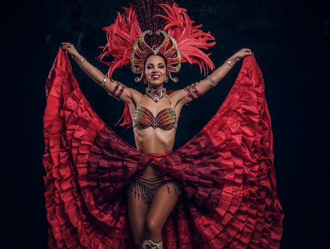Talented joyful can can dancer in red feather costume is posing at small dark studio.