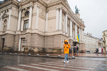 woman in orange raincoat crossing road old european building on background
