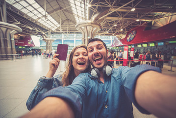 Obraz na płótnie Canvas Beautiful young tourist couple in international airport, taking selfie with passport and boarding pass ready for boarding in the airplane and fly. Travel around the world concept.