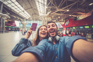 Obraz na płótnie Canvas Beautiful young tourist couple in international airport, taking selfie with passport and boarding pass ready for boarding in the airplane and fly. Travel around the world concept.