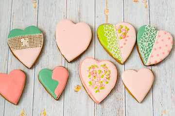 Fototapeta premium Pink and colored gingerbread and honey cakes and biscuits. Heart-shaped lie on a light wooden background. Patern. Place for text. The concept of love, mother's day, cooking,