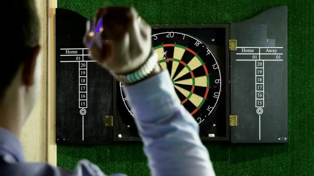 Man throwing a dart arrow in target center of dartboard in game of darts. 4K