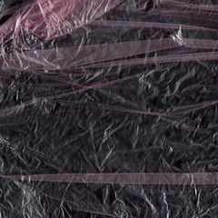 Transparent plastic wrap on the black background. Plastic bag texture. Reusable trash and waste.