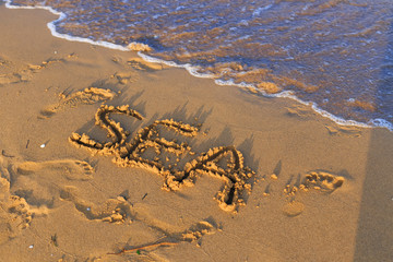 Fototapeta na wymiar The sea is written on wet sand on the beach with waves