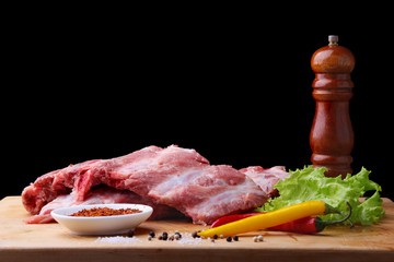 Raw Ribs on a rustic cutting board with salt, pepper and grinder for spices . Black Background for copy space. Top View.