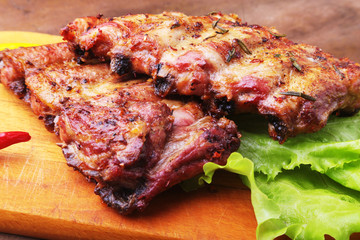 grilled barbecued ribs with lettuce leaves, hot chili pepper and sauce on wooden cutting board.
