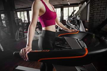 Fototapeta na wymiar Young pretty woman running on treadmill. Loft interior of modern fitness club in black colour. Concept of health and sport lifestyle. Athletic Body.