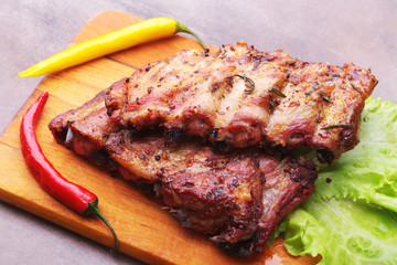 grilled barbecued ribs with lettuce leaves, hot chili pepper and sauce on wooden cutting board.