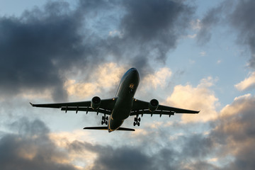 Travel, transportation, aviation concept. Silhouette of wide-body passenger airplane flying overhead after take off against a evening cloudy sky at sunset, bottom view