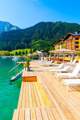 Pier with chairs on sunny terrace on shore of beautiful Achensee lake on sunny summer day with blue sky, Karwendel mountain range, Tirol, Austria