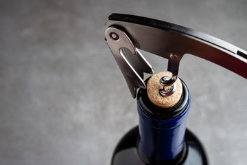 Bottle of wine with corkscrew on concrete background.