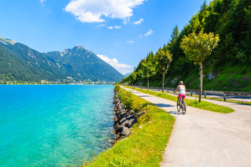 Young woman tourist riding bike along Achensee lake on sunny summer day, Pertisau, Tirol, Austria