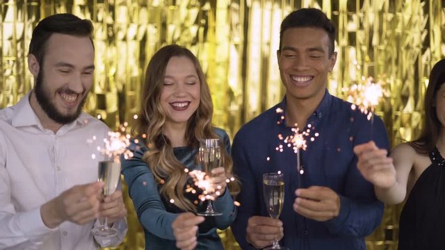 4 happy cheerful people at a party light a sparkler. a group of laughing people of mixed race on a gold background. 4K