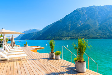 Pier with chairs on sunny terrace on shore of beautiful Achensee lake on sunny summer day with blue sky, Karwendel mountain range, Tirol, Austria