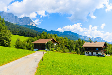 Road and traditional alpine houses in village of Going am Wilden Kaiser on beautiful sunny summer day with Alps mountains in background, Tirol, Austria