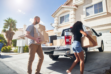 interracial couple moving into new home and taking boxes out of truck
