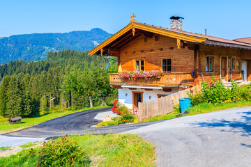 Typical wooden alpine house decorated with flowers on green meadow in Reith village on sunny summer...