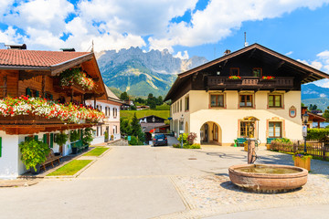 Obraz premium Traditional alpine houses on square in village of Going am Wilden Kaiser on beautiful sunny summer day with Alps mountains in background, Tirol, Austria