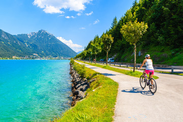 Young woman tourist riding bike along Achensee lake on sunny summer day, Pertisau, Tirol, Austria