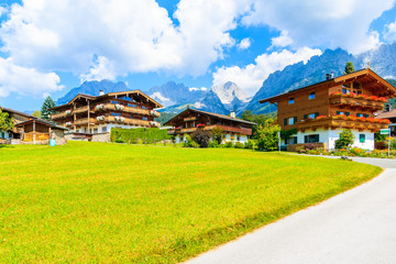 Road and traditional alpine houses in village of Going am Wilden Kaiser on beautiful sunny summer day with Alps mountains in background, Tirol, Austria