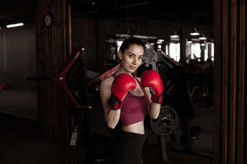 Young pretty woman in red boxing gloves on a background of the gym.