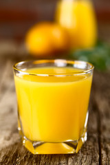 Orange juice in glass on rustic wood (Selective Focus, Focus on the front of the glass rim)