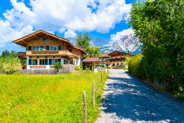 Road and traditional alpine houses in village of Going am Wilden Kaiser on beautiful sunny summer day with Alps mountains in background, Tirol, Austria