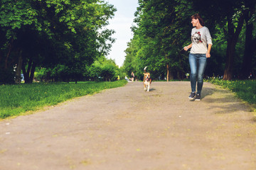 Obraz premium Girl running with her cute female beagle dog in the park at summer time. Lifestyle photo.