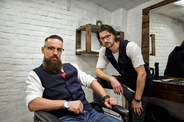 Brutal guy in modern Barber Shop. Hairdresser makes hairstyle a man with a long beard. Master hairdresser does hairstyle by scissors and comb