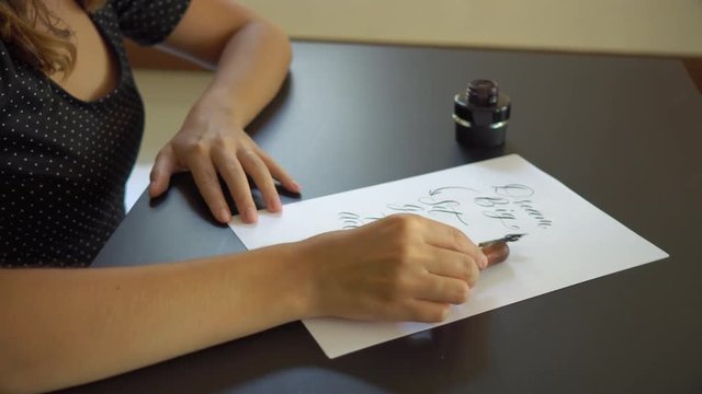 Close up shot of a young woman calligraphy writing on a paper using lettering technique. She writtes Dream big Set goals Take action