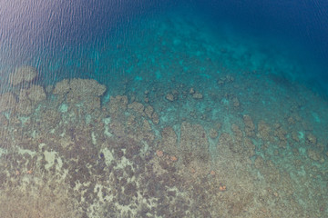 Seen from a bird's eye view, a coral reef grows along the coastline of Flores, Indonesia. This tropical area is known for its marine biodiversity as well as its volcanic activity.
