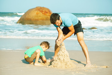 happy family on beach playing, father with son walking sea coast, rocks behind smiling taking vacation
